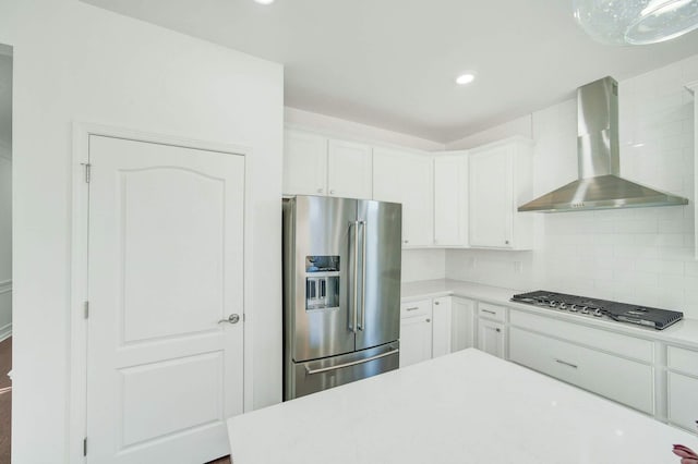 kitchen featuring tasteful backsplash, white cabinets, stainless steel appliances, and wall chimney range hood