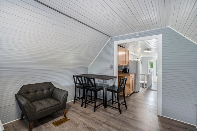 dining room with wooden walls, hardwood / wood-style floors, wood ceiling, and vaulted ceiling