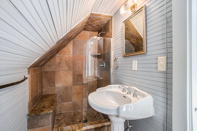 bathroom with a tile shower, wooden walls, sink, wooden ceiling, and lofted ceiling