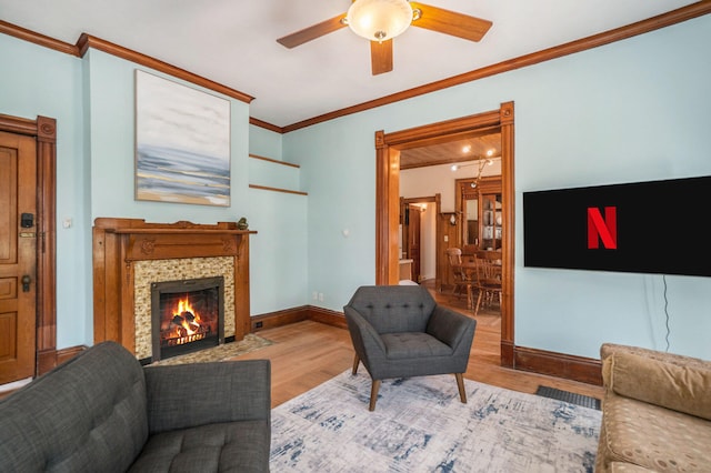 living room featuring ceiling fan, a fireplace, ornamental molding, and light wood-type flooring