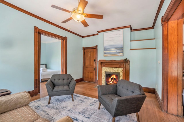 living room featuring ceiling fan, a fireplace, crown molding, and light wood-type flooring