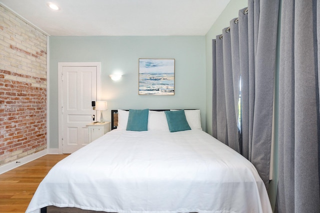 bedroom featuring wood-type flooring and brick wall