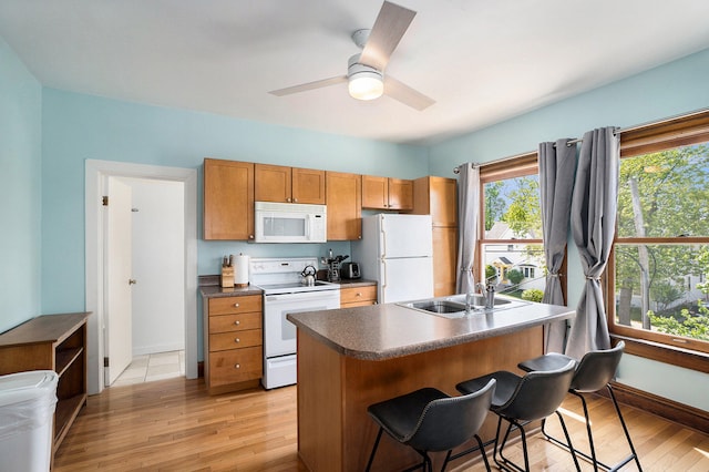 kitchen with light wood-type flooring, a breakfast bar, white appliances, ceiling fan, and sink