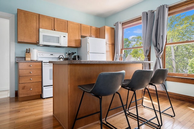 kitchen featuring a breakfast bar, light hardwood / wood-style flooring, and white appliances