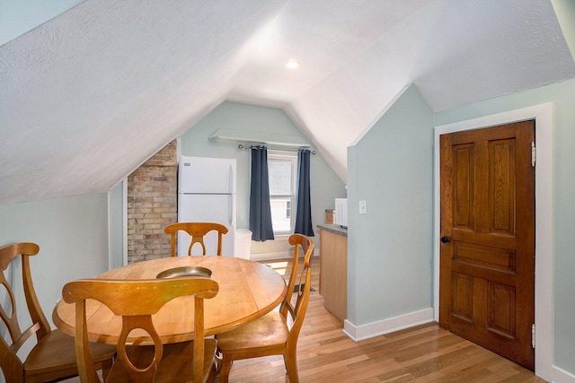 dining room with a textured ceiling, light hardwood / wood-style floors, and vaulted ceiling