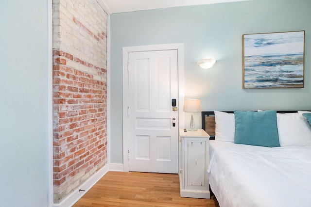 bedroom featuring light hardwood / wood-style flooring and brick wall