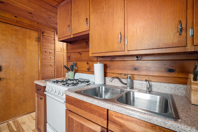 kitchen featuring custom exhaust hood, sink, wooden walls, light hardwood / wood-style flooring, and white range with gas stovetop