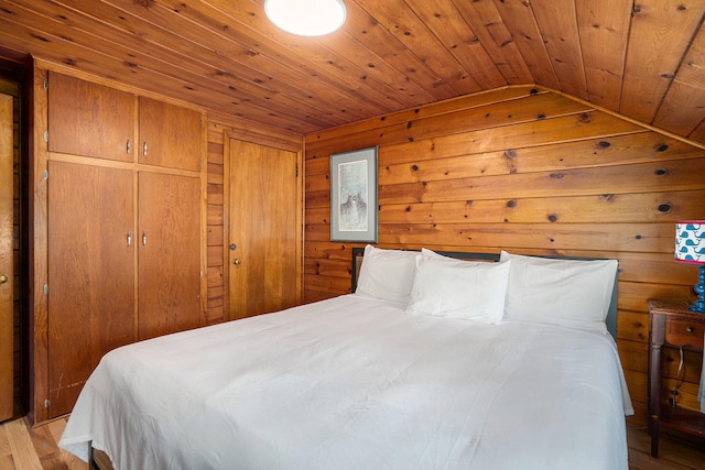 bedroom featuring wood ceiling, wood walls, light hardwood / wood-style floors, and lofted ceiling