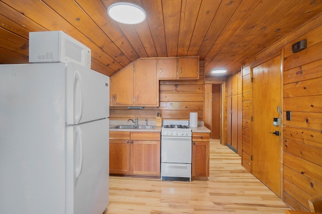 kitchen featuring wood walls, light hardwood / wood-style flooring, white appliances, and sink