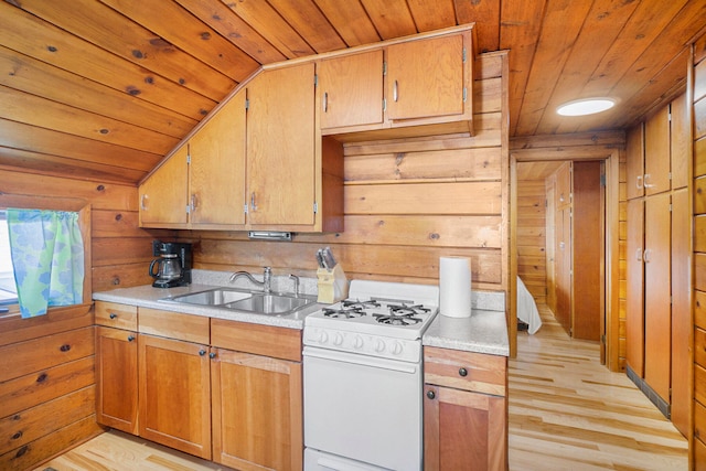 kitchen with vaulted ceiling, white range with gas cooktop, wooden walls, sink, and light hardwood / wood-style flooring