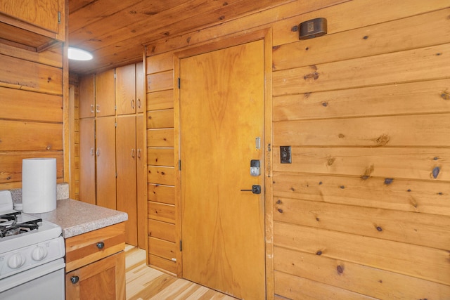 kitchen featuring white range with gas stovetop, light hardwood / wood-style flooring, and wooden walls