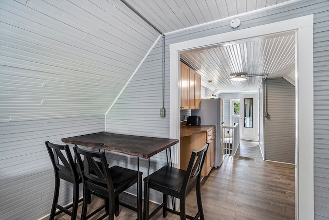 dining area featuring hardwood / wood-style floors, wooden ceiling, vaulted ceiling, and wooden walls