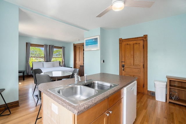 kitchen with ceiling fan, dishwasher, sink, light hardwood / wood-style floors, and a center island with sink