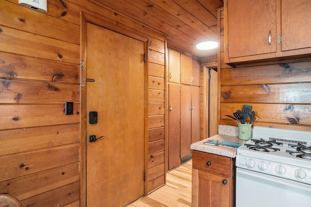 kitchen featuring white range with gas cooktop, wooden walls, wooden ceiling, and light wood-type flooring