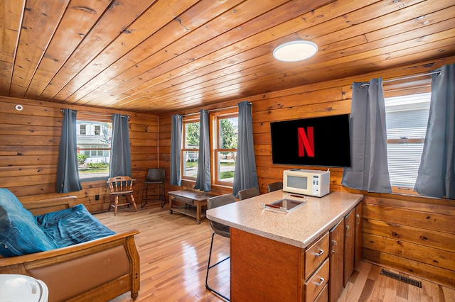 interior space featuring wood walls, light hardwood / wood-style floors, a kitchen island, and wooden ceiling