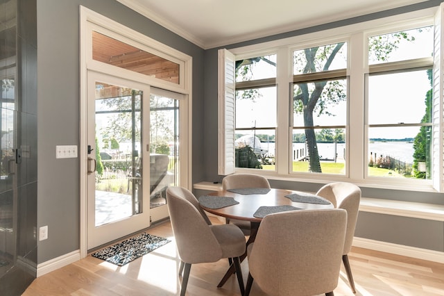 dining area with a water view, a wealth of natural light, light wood-style flooring, and crown molding