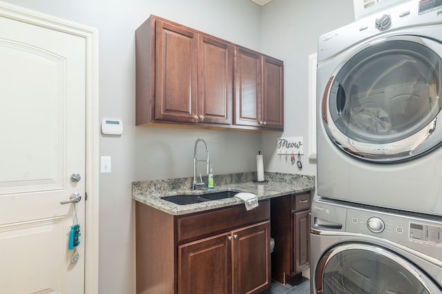 clothes washing area featuring a sink, stacked washer and dryer, and cabinet space