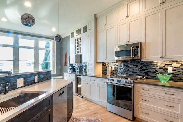 kitchen featuring wine cooler, appliances with stainless steel finishes, a sink, light wood-type flooring, and backsplash