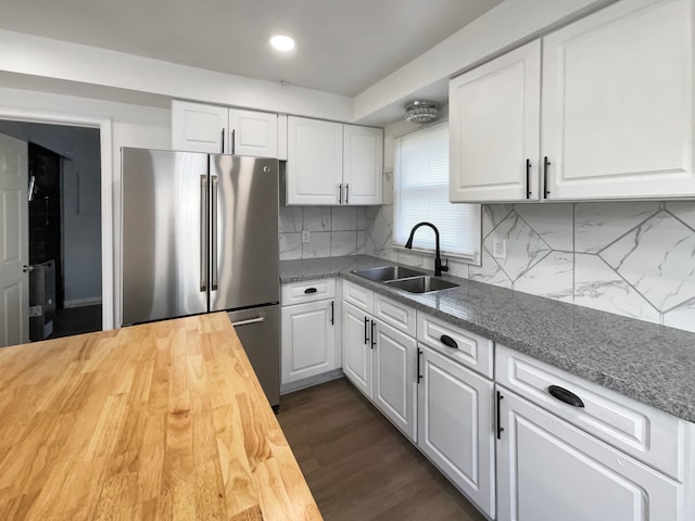 kitchen with decorative backsplash, wood counters, sink, white cabinets, and stainless steel refrigerator