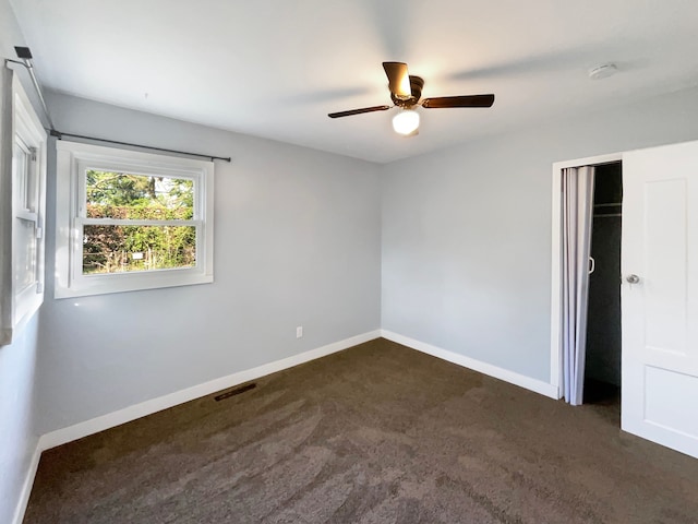 unfurnished bedroom featuring ceiling fan, a closet, and dark colored carpet