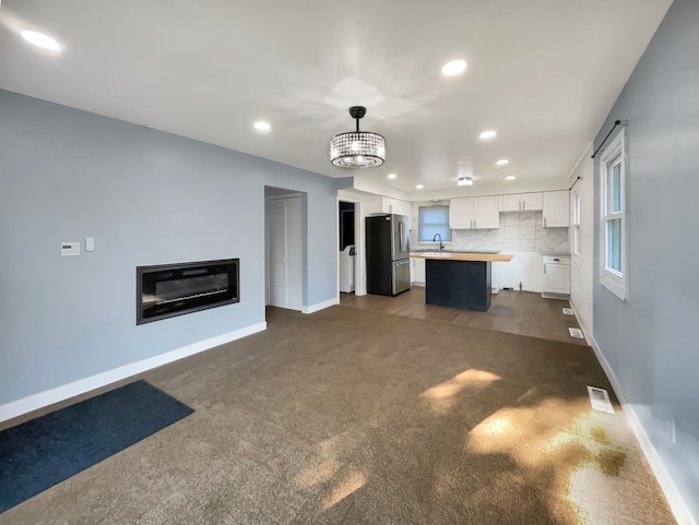 unfurnished living room with dark carpet, sink, and an inviting chandelier