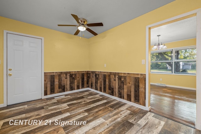 unfurnished room with wooden walls, ceiling fan with notable chandelier, and hardwood / wood-style flooring