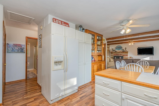 kitchen featuring white cabinetry, a fireplace, white refrigerator with ice dispenser, and light wood-type flooring