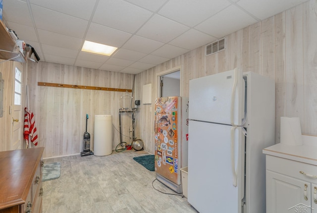 kitchen featuring wooden walls, white refrigerator, light hardwood / wood-style floors, and a paneled ceiling