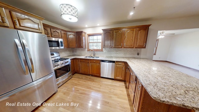 kitchen with kitchen peninsula, appliances with stainless steel finishes, light wood-type flooring, ceiling fan, and sink