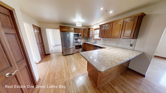 kitchen featuring sink, light stone countertops, light hardwood / wood-style floors, kitchen peninsula, and stainless steel appliances