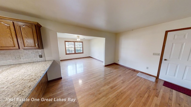 interior space with ceiling fan, light stone countertops, light wood-type flooring, and tasteful backsplash