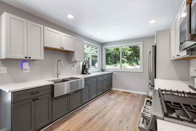 kitchen with sink, light wood-type flooring, gray cabinets, white cabinets, and appliances with stainless steel finishes