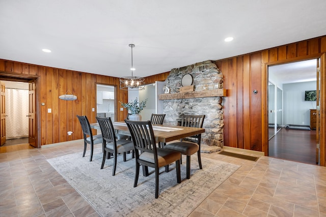 dining room with a stone fireplace, a notable chandelier, and wood walls