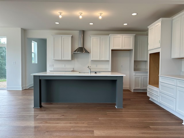 kitchen with wall chimney exhaust hood, sink, a center island with sink, light hardwood / wood-style flooring, and white cabinets