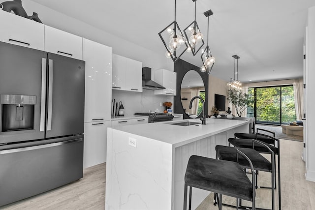 kitchen featuring a center island with sink, sink, light wood-type flooring, appliances with stainless steel finishes, and decorative light fixtures