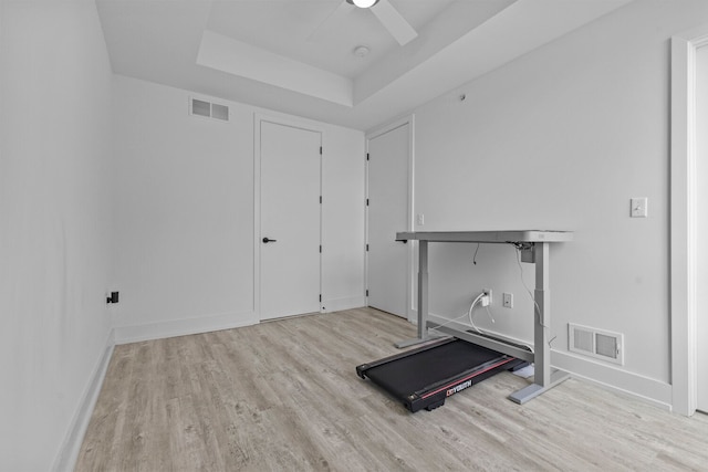 exercise room with ceiling fan, a raised ceiling, and light wood-type flooring