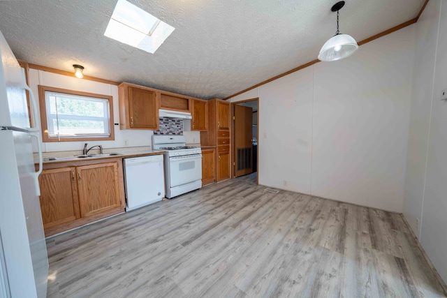 kitchen with a skylight, white appliances, sink, pendant lighting, and light hardwood / wood-style floors