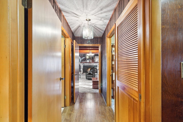 hallway with wood-type flooring, wooden walls, a textured ceiling, and a notable chandelier