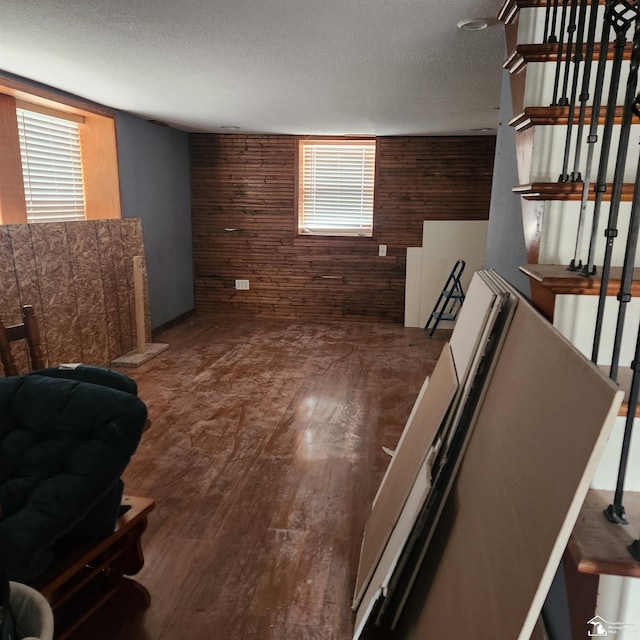 basement featuring plenty of natural light, wooden walls, dark hardwood / wood-style flooring, and a textured ceiling