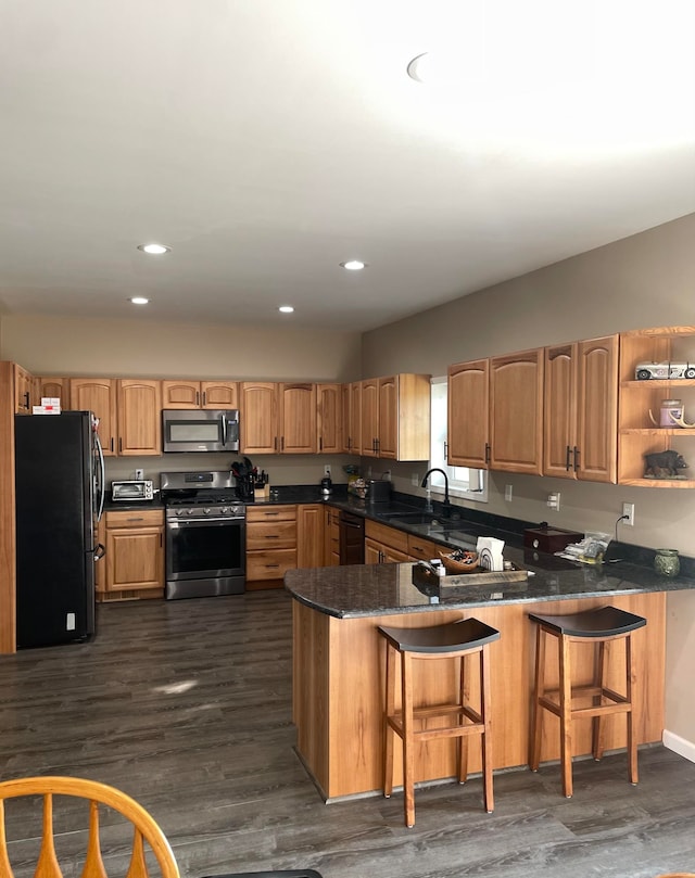 kitchen featuring dark wood-type flooring, black appliances, sink, a kitchen bar, and kitchen peninsula