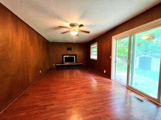 unfurnished living room with hardwood / wood-style floors, ceiling fan, and wood walls