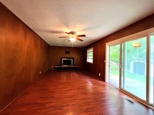 unfurnished living room with wood walls, ceiling fan, and dark wood-type flooring