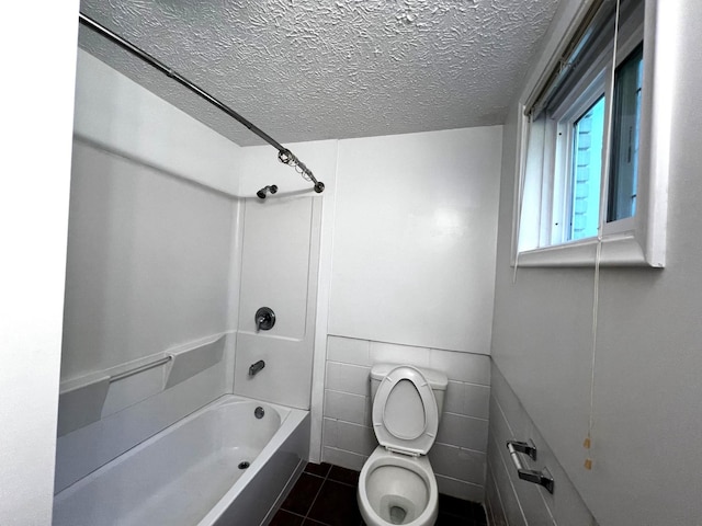 bathroom with bathtub / shower combination, tile patterned flooring, toilet, a textured ceiling, and tile walls