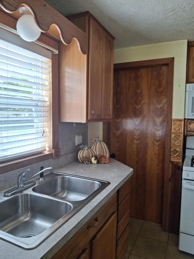 kitchen featuring a textured ceiling, light tile patterned flooring, white appliances, and sink