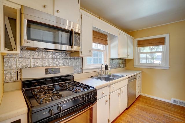 kitchen featuring sink, light hardwood / wood-style flooring, backsplash, white cabinets, and appliances with stainless steel finishes