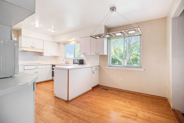 kitchen with kitchen peninsula, cooktop, light hardwood / wood-style flooring, and white cabinetry