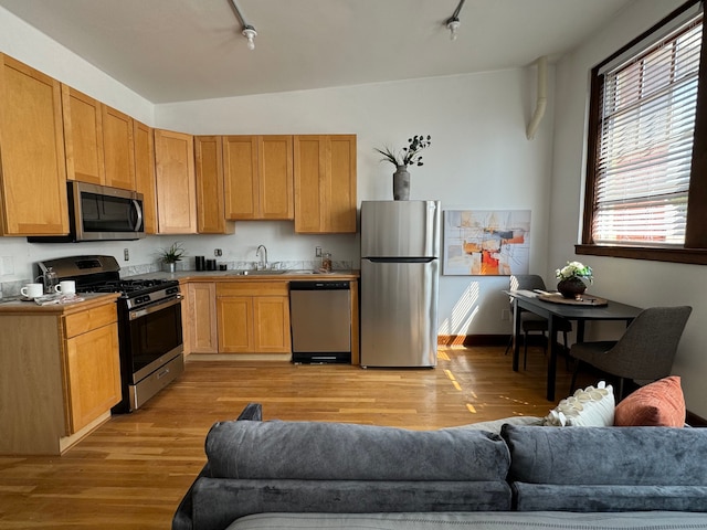 kitchen featuring vaulted ceiling, stainless steel appliances, track lighting, and light hardwood / wood-style flooring