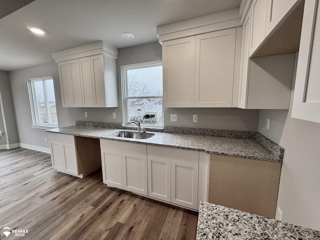 kitchen with white cabinetry, light hardwood / wood-style floors, sink, and light stone counters