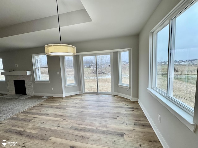 unfurnished dining area featuring a brick fireplace, a wealth of natural light, and light hardwood / wood-style floors