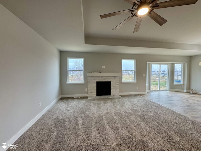 unfurnished living room with ceiling fan, light colored carpet, a tray ceiling, and a wealth of natural light